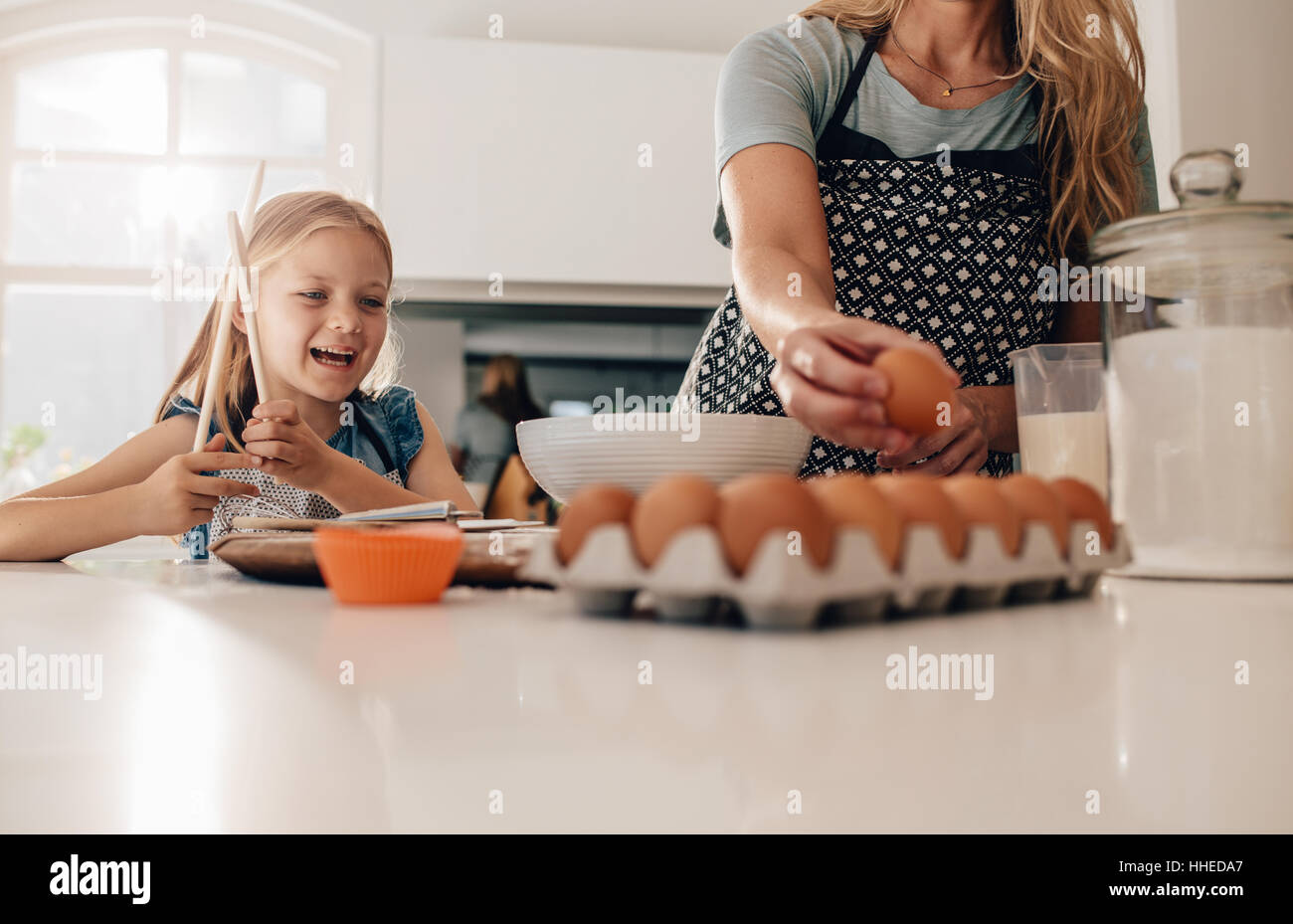 Bambina in piedi in cucina con la madre la cottura. La donna la raccolta delle uova e la figlia in piedi dalla sorridente. Foto Stock