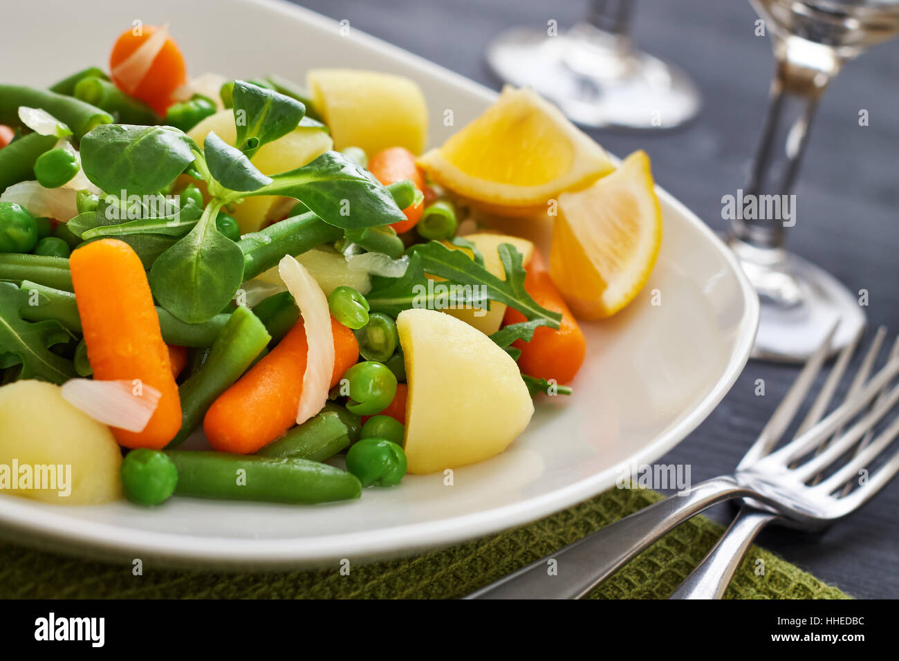 Insalata con baby carote, piselli, cipolle e patate servita su piastra di bianco su nero lo sfondo di legno Foto Stock