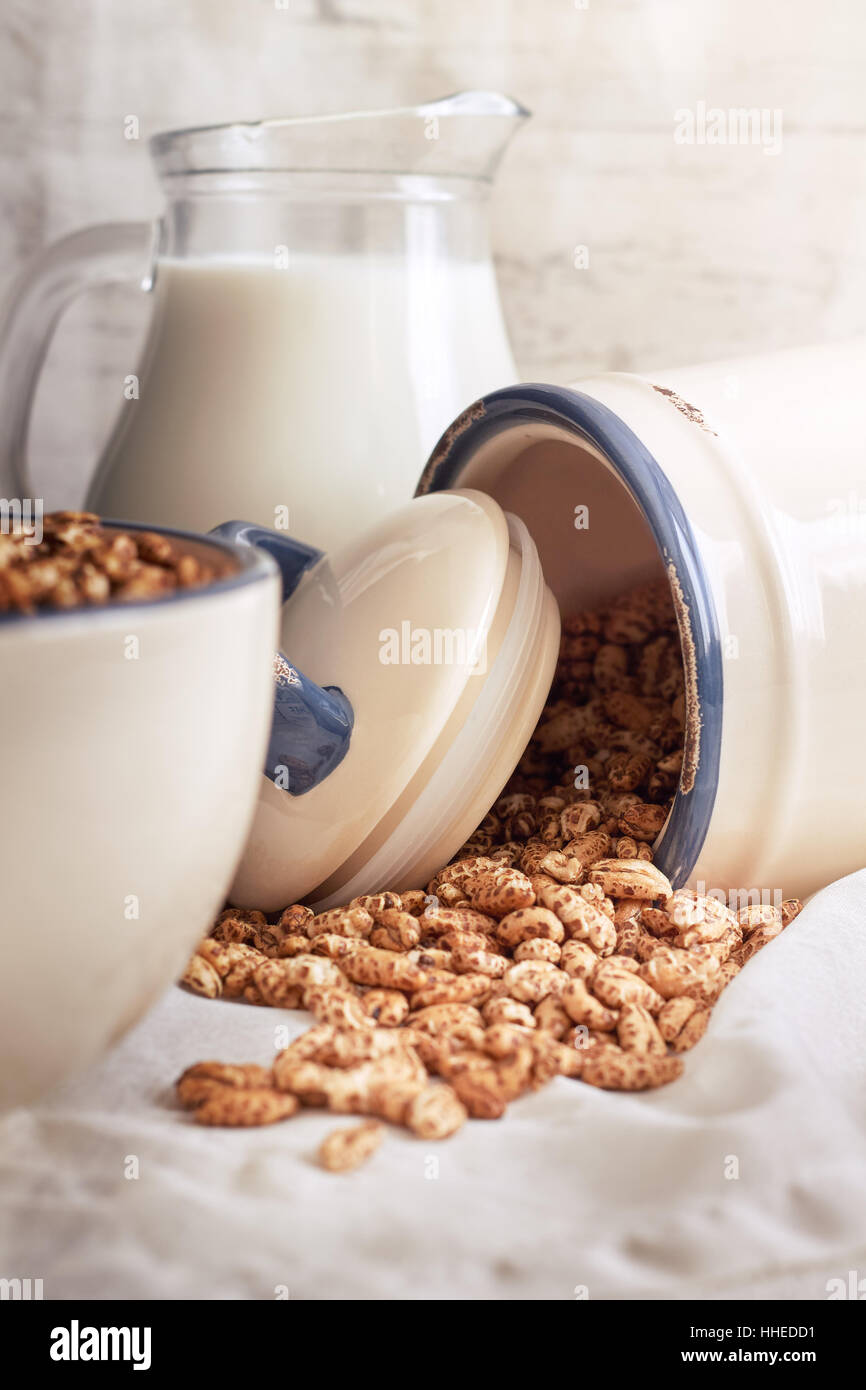 Orzo soffiato sversamento di cereali da jar con la brocca del latte in background Foto Stock
