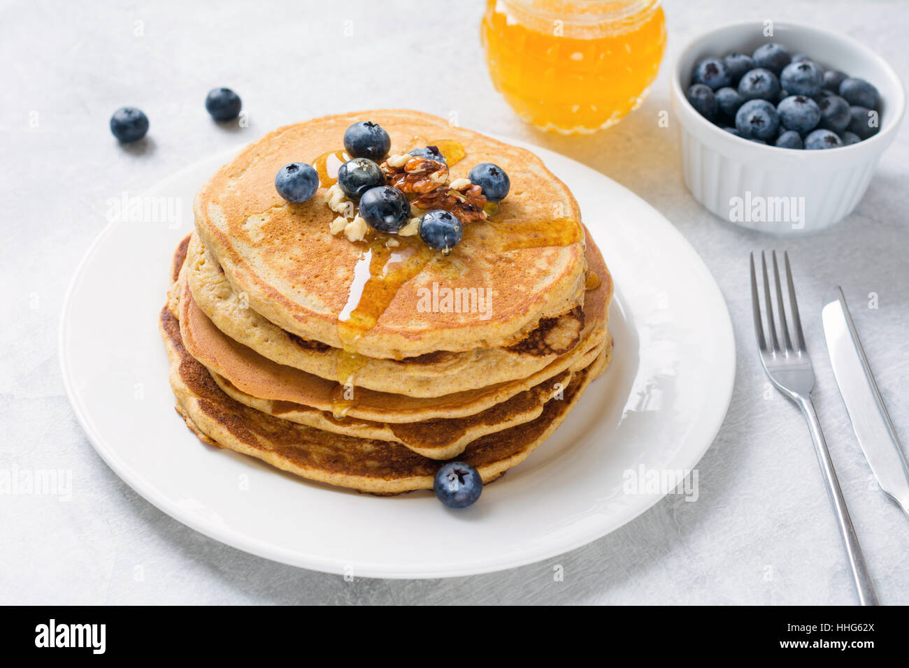Pila di pancake con mirtilli freschi, noci e miele sulla piastra bianca. Una sana prima colazione il cibo. Primo piano vista laterale Foto Stock