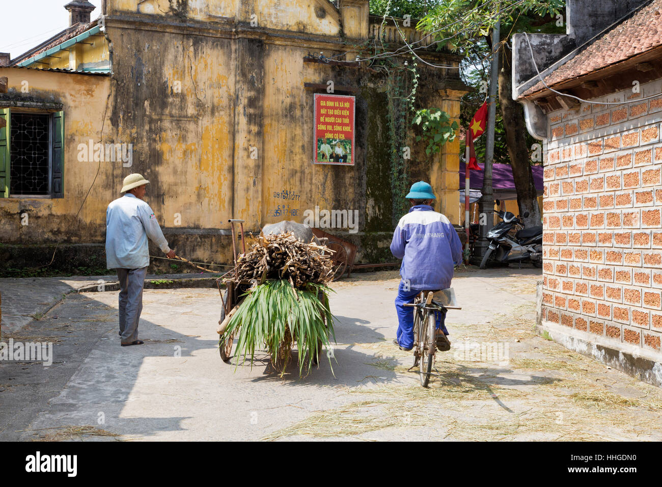 Agricoltore passeggiando per il borgo, portando il bufalo d'acqua, tirando il carrello portante raccolti vegetali, membro della famiglia in bicicletta lungo. Foto Stock