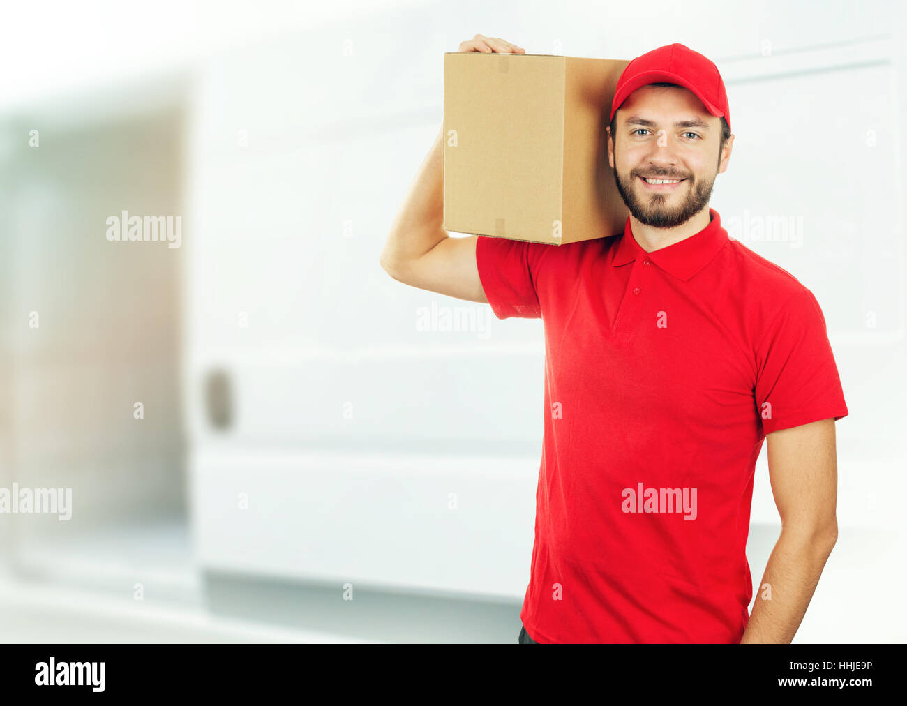 Felice l'uomo di consegna con scatola sullo spallamento nella parte anteriore del carrello Foto Stock