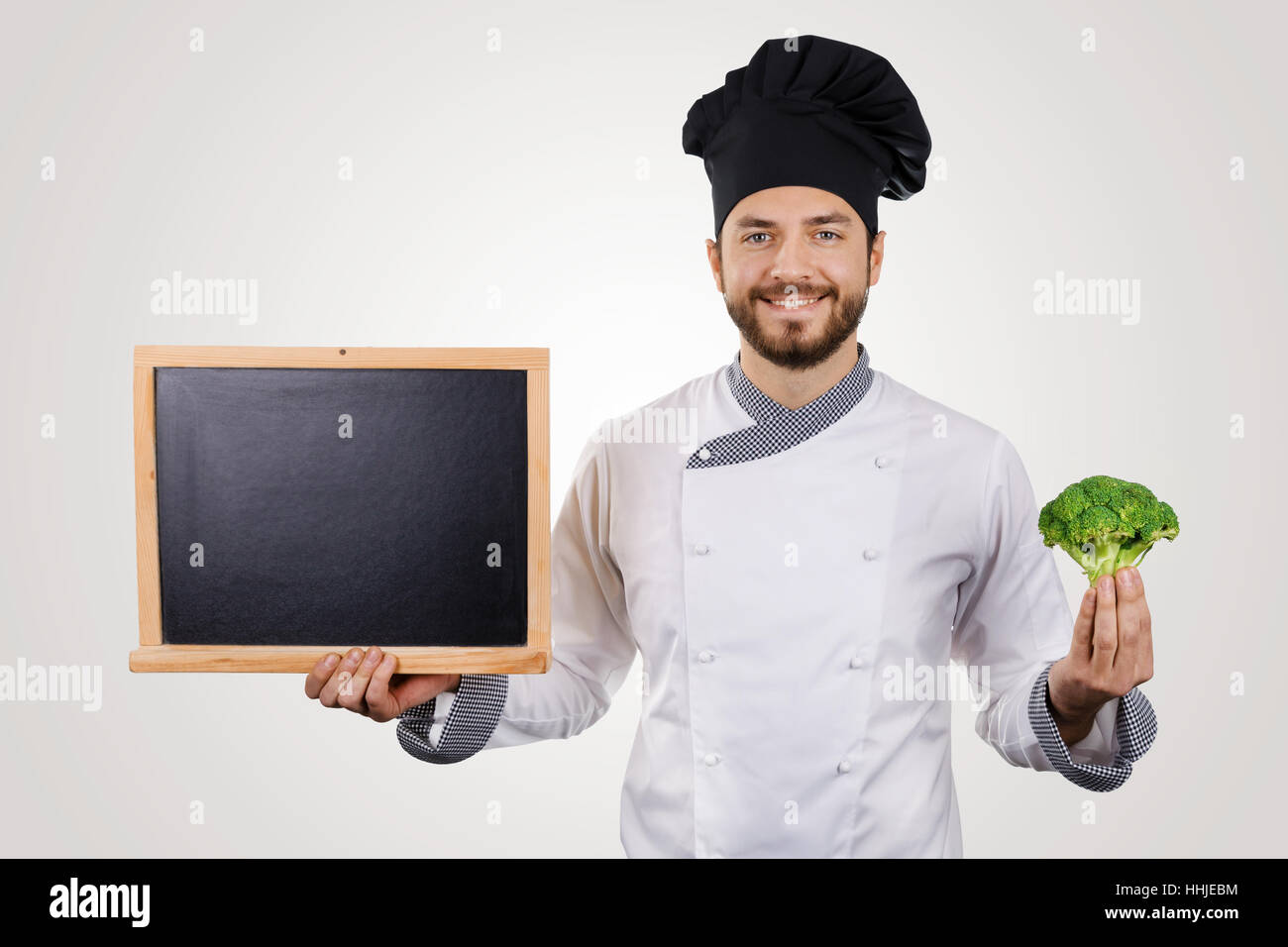 Sorridente giovane chef con lavagna vuota e broccoli in mano Foto Stock