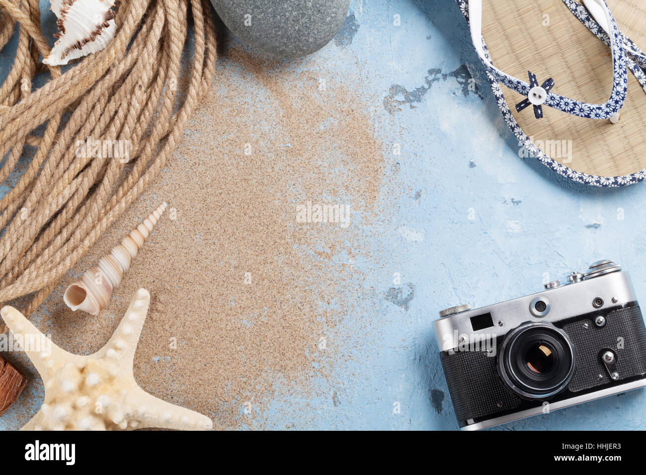 Vacanza al mare sullo sfondo. Fotocamera, stelle marine e flip-flop su uno sfondo di pietra con sabbia. Vista da sopra con copia spazio. Foto Stock
