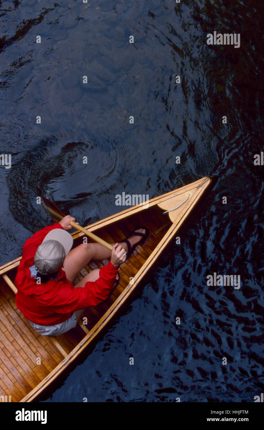 Una giovane donna nella sua 20's indossando un luminoso red jacket pagaie la sua annata canoe di legno in un flusso di acque bianche Foto Stock