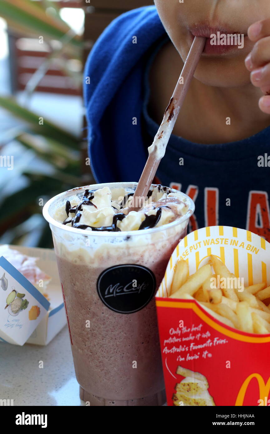 Close up di un bambino bere McDonald's cioccolato Frappé e mangiare patatine in McDonald's Melbourne Victoria Australia Foto Stock