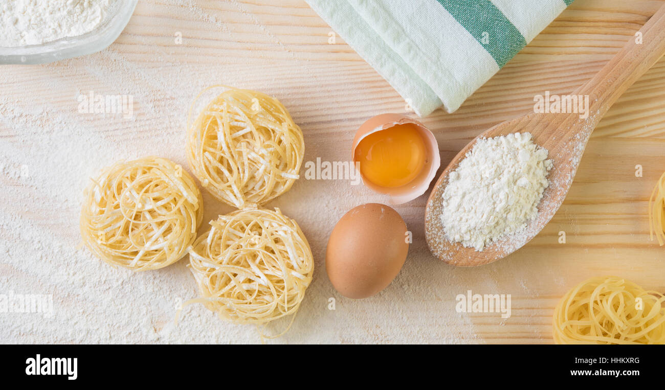 Preparazione della tradizionale italiana tagliatelle fatte in casa pasta con farina e uova su una tavola di legno Foto Stock