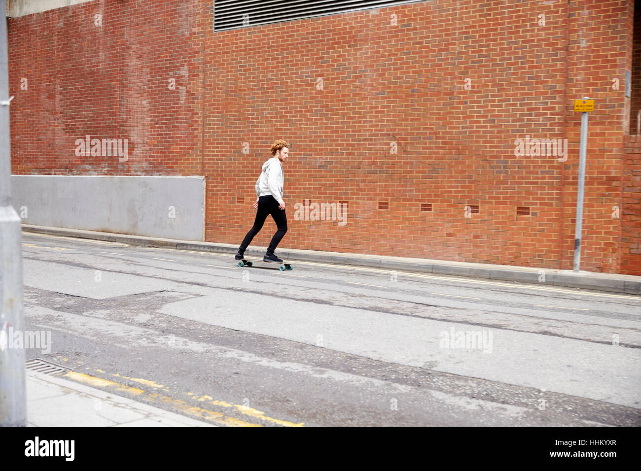 Dai capelli rossi uomo lo skateboard su una strada urbana, vista laterale Foto Stock