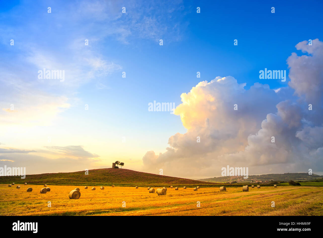 Toscana La Maremma tipico paesaggio paesaggio al tramonto e tempesta cloud. Hill, alberi, le balle di paglia e torre rurale. Foto Stock