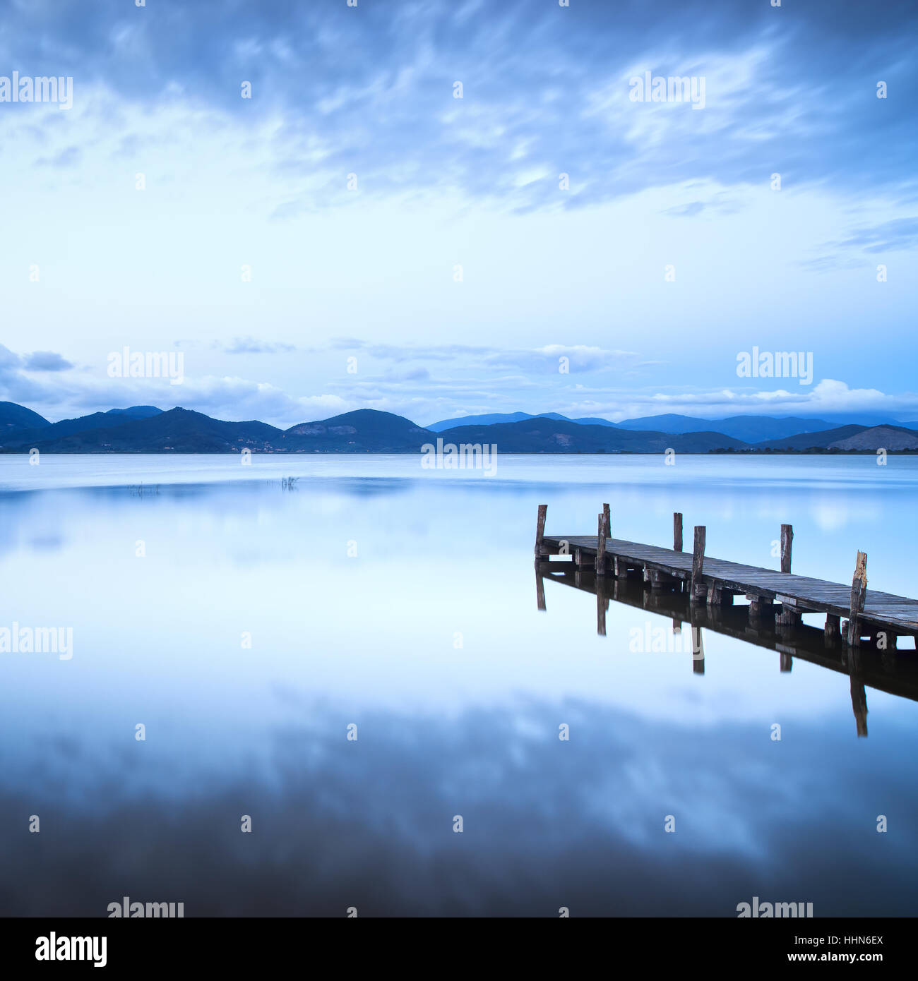 Il molo di legno o un pontile e su un lago blu tramonto e il cielo nuvoloso la riflessione sull'acqua. Una lunga esposizione, Versilia Lago di Massaciuccoli, Toscana, Italia. Foto Stock