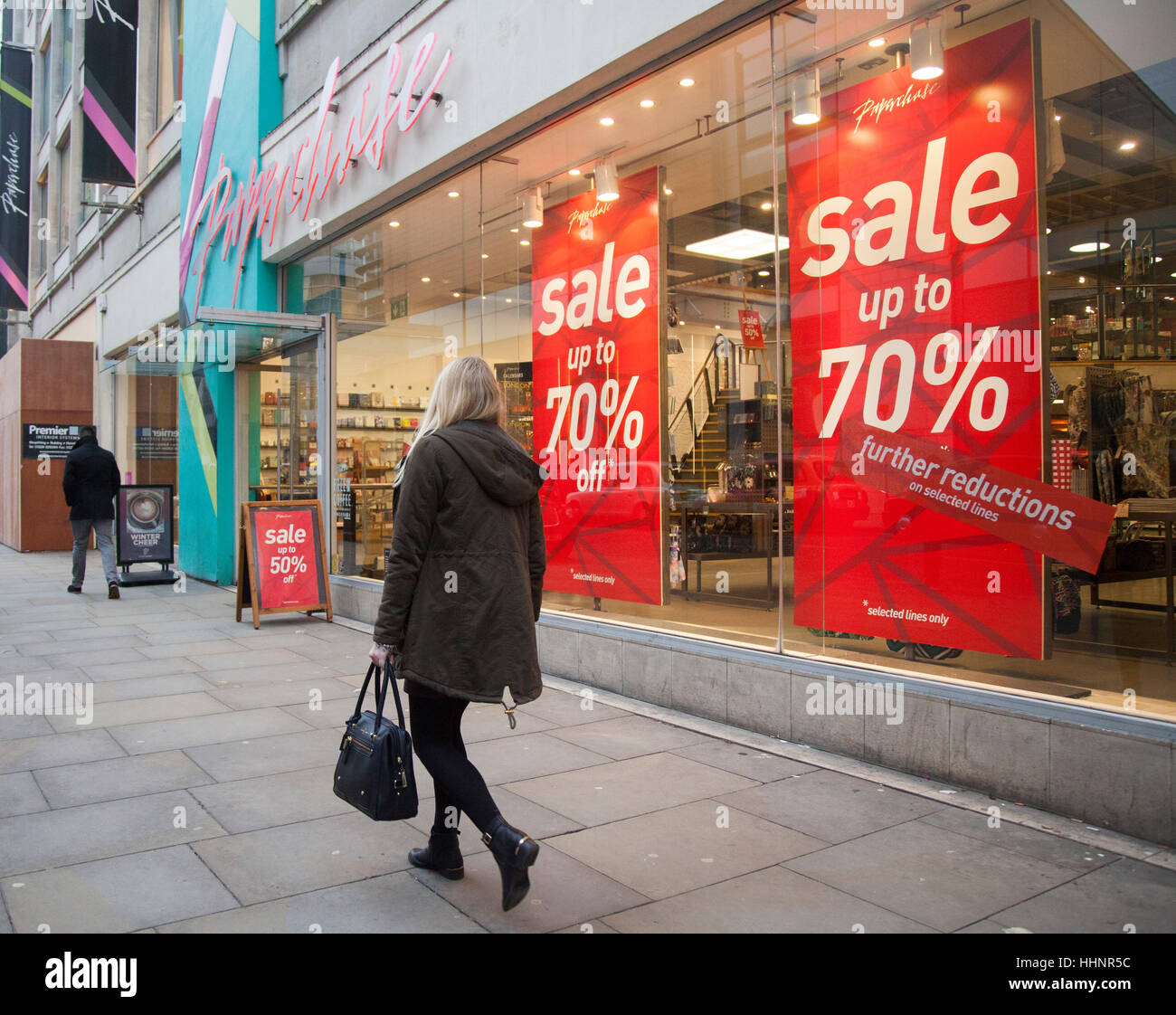 Donna che passa davanti al negozio di cartoleria Paperchase negozi 'fino al 70% di sconto' sconti poster, ulteriori riduzioni a Manchester, Regno Unito Foto Stock