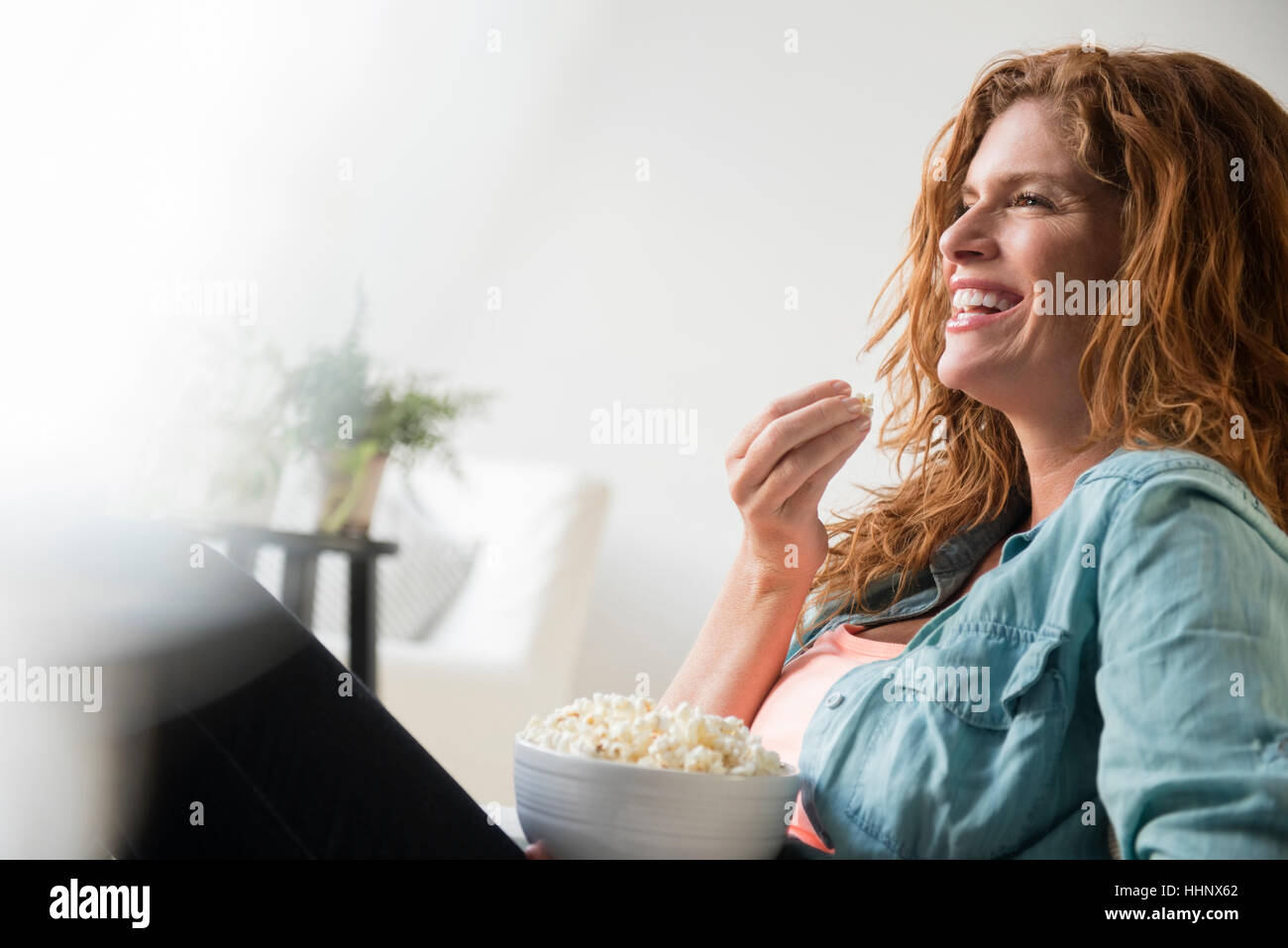 Ridendo donna caucasica mangiare una ciotola di pop-corn Foto Stock