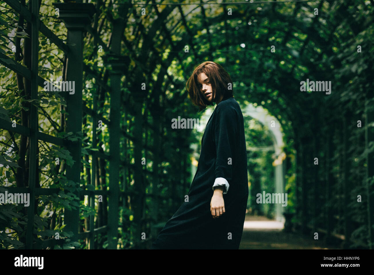 La donna caucasica indossando abito nero sotto il fogliame Foto Stock