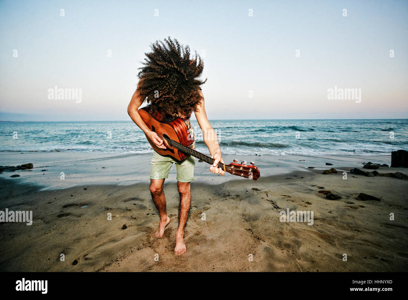 Razza mista uomo tossing capelli e suonare la chitarra in spiaggia Foto Stock