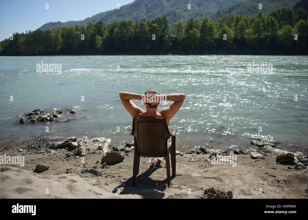 Uomo caucasico seduto in poltrona a prendere il sole vicino al fiume Foto Stock