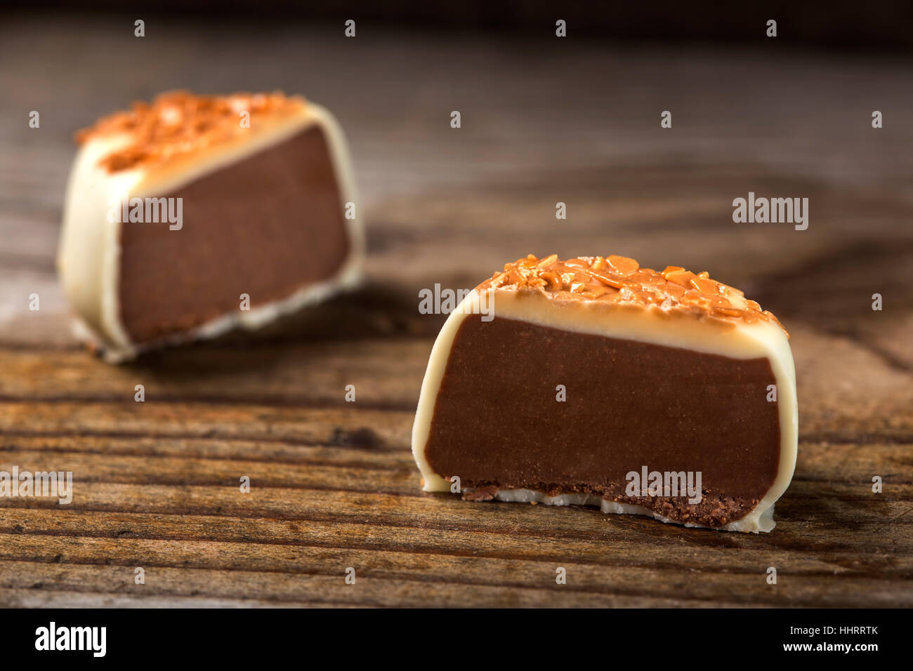 Una scatola di cioccolatini tagliato a metà con piccoli pezzi di caramello su sfondo di legno Foto Stock