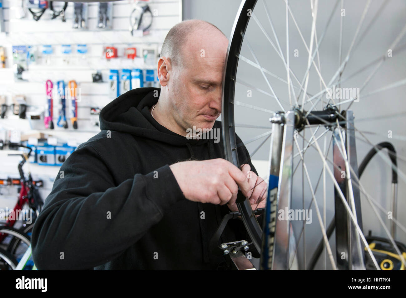 Un meccanico di bicicletta la centratura di una ruota posteriore nel suo laboratorio. Foto Stock