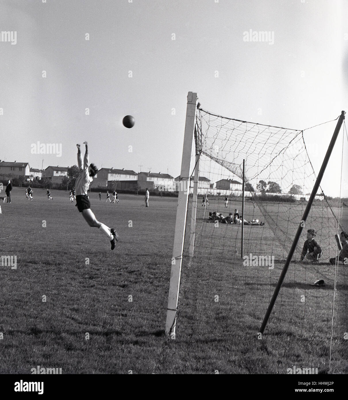 Anni sessanta, storico di calcio amatoriale corrispondono, salta il portiere ma la palla è sul punto di andare in net di segnare un gol o sta andando oltre la barra?......renderebbe un buon posto la sfera della concorrenza. Foto Stock