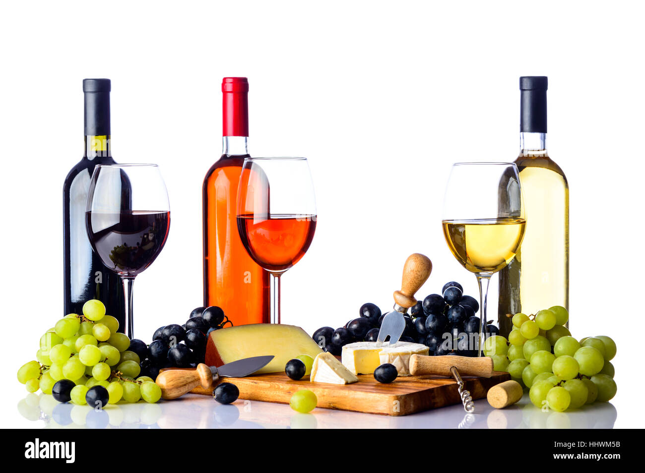 Tre Bicchieri e bottiglie di vino con uve bianche e rosse, formaggi e sul tagliere di legno, tutti su sfondo bianco Foto Stock