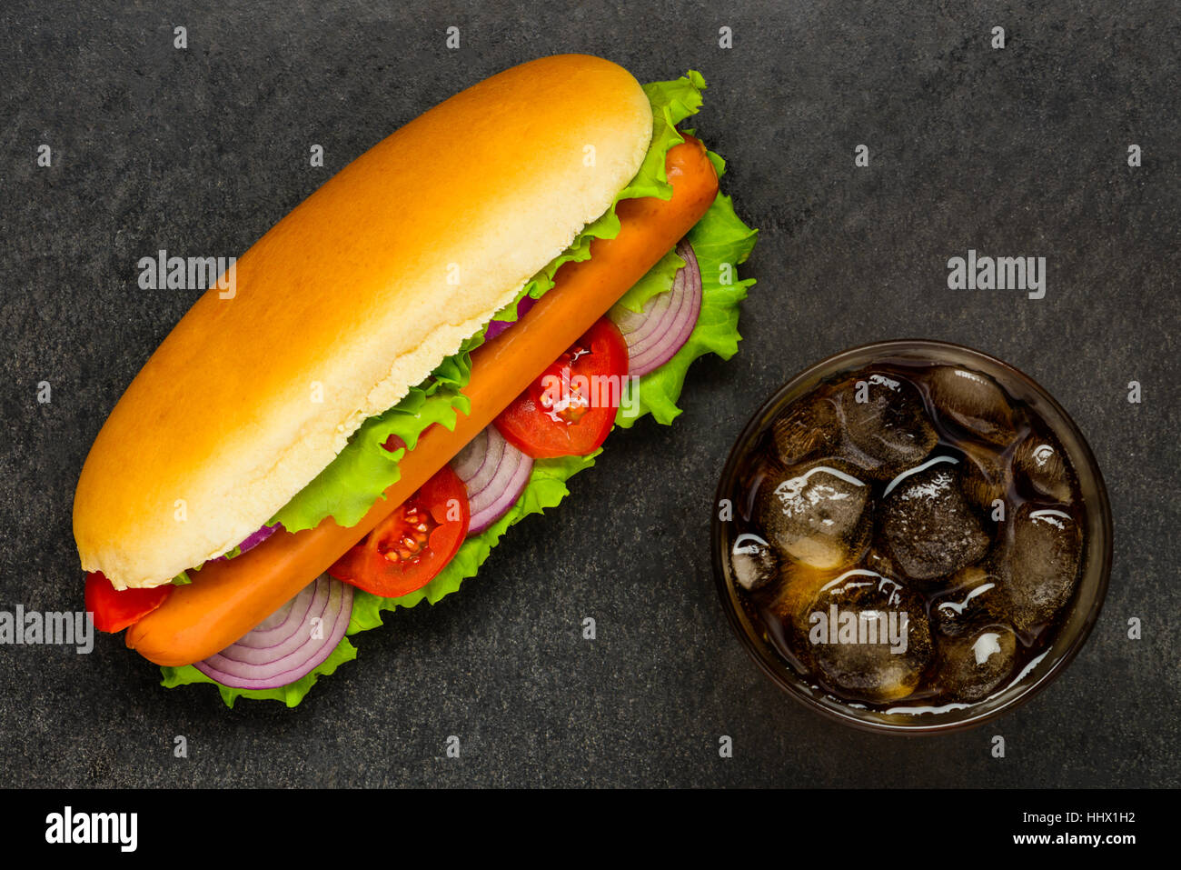 Hot Dog panino con salsiccia e verdure fresche al buio su un tavolo con vetro Cola a freddo Foto Stock