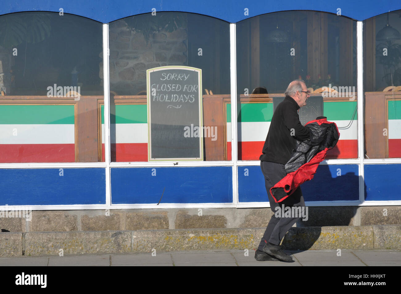 Un uomo in fretta camminare davanti a un caffè chiuso per l'inverno in Cornovaglia. Foto Stock