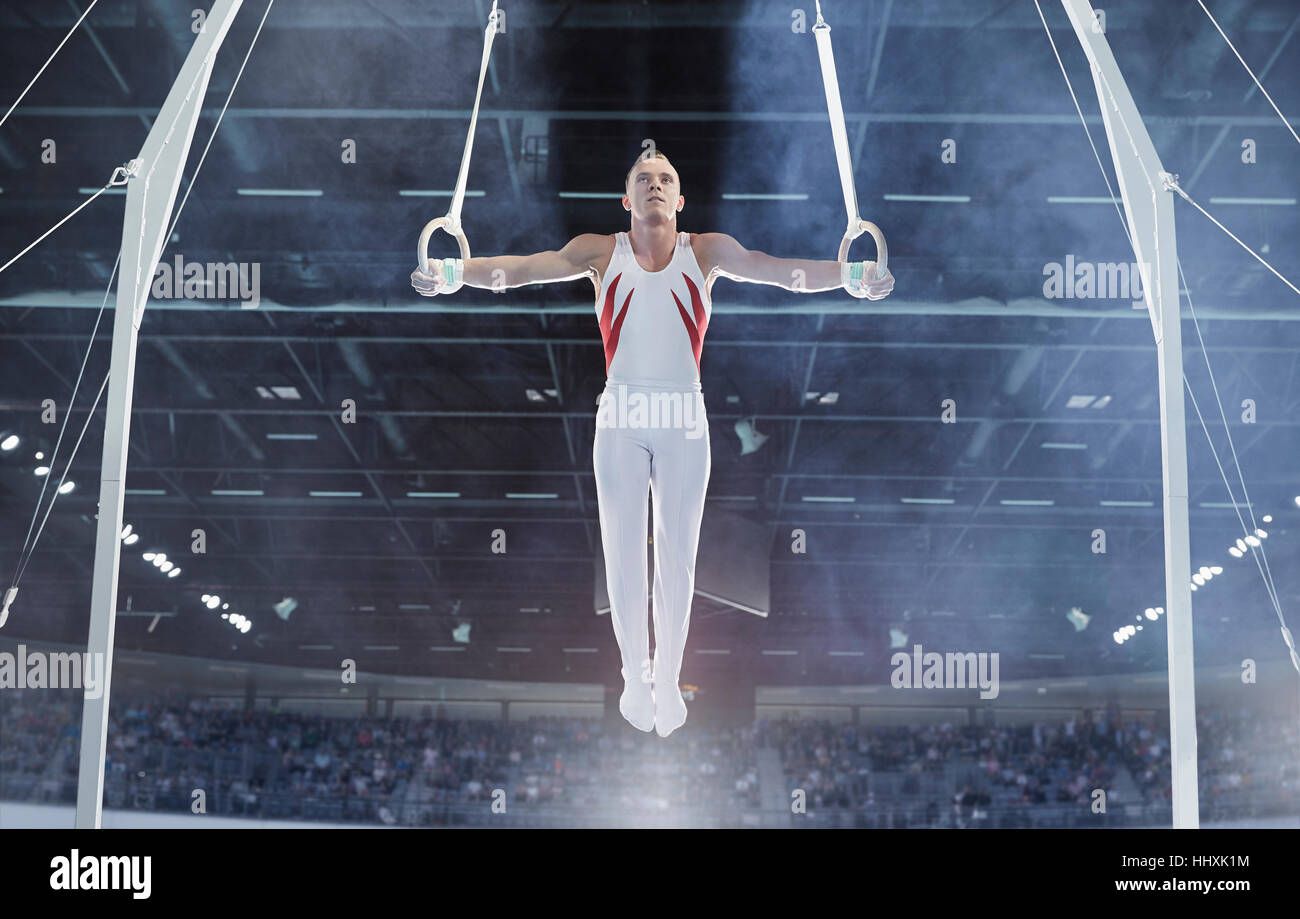Maschio di bilanciamento del ginnasta con braccia tese su anelli di ginnastica in arena Foto Stock