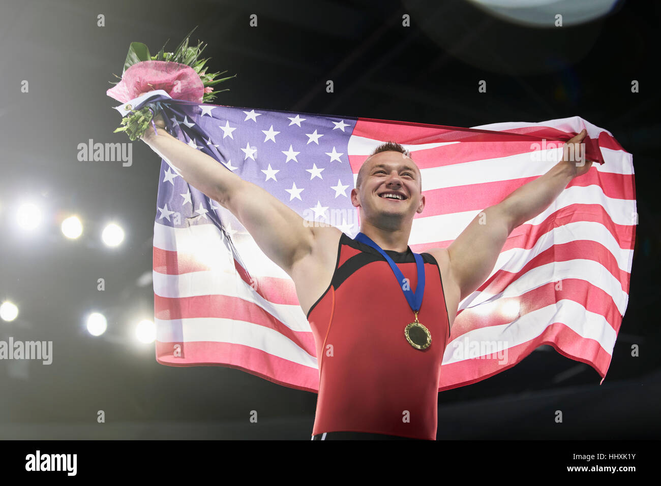 Entusiasta ginnasta maschio celebrando la vittoria holding bandiera americana sul podio dei vincitori Foto Stock
