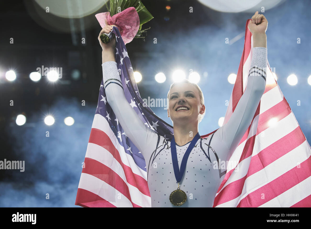 Entusiasta ginnasta femmina celebrando la vittoria holding bandiera americana sul podio dei vincitori Foto Stock