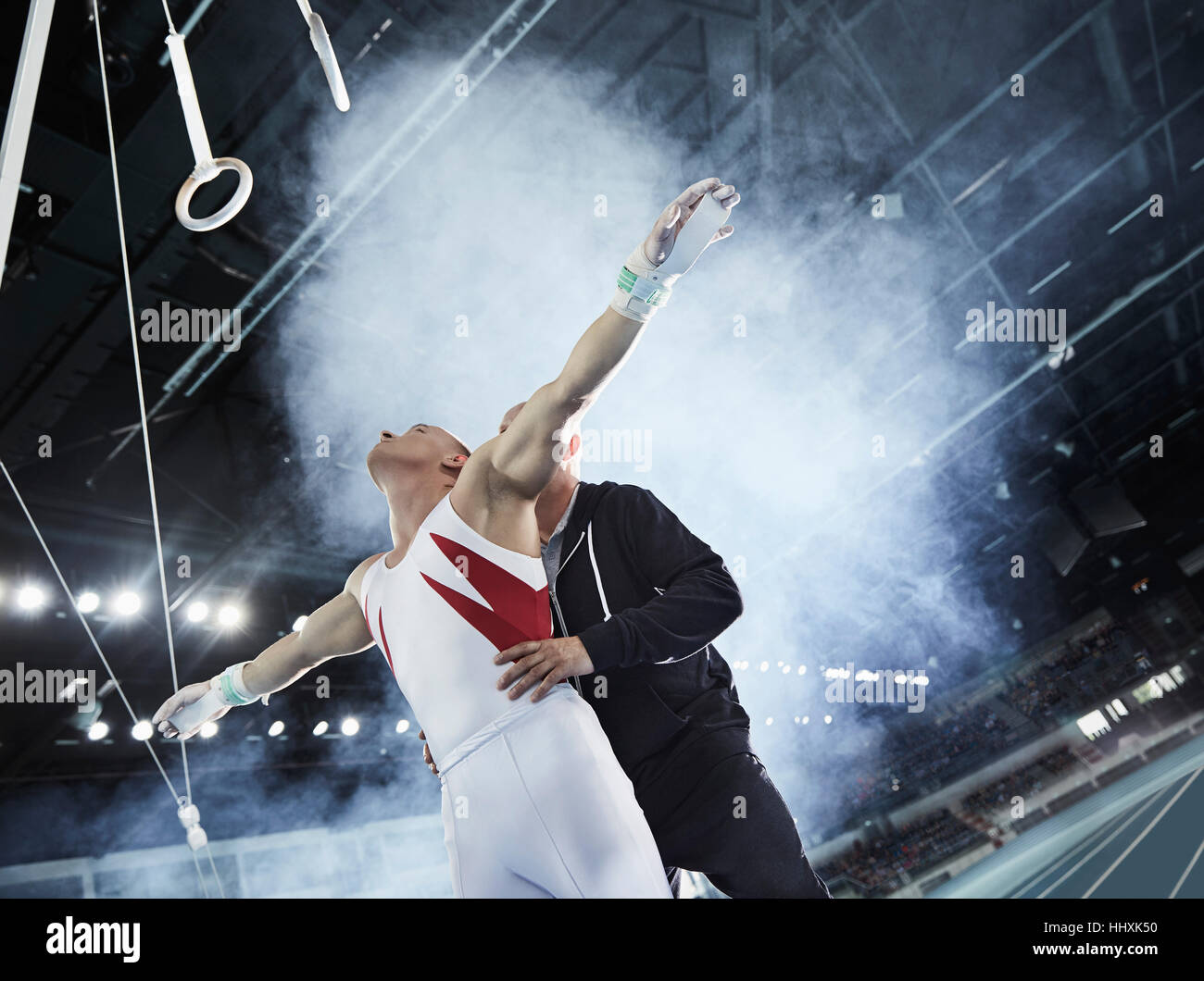 Pullman di sollevamento ginnasta maschio sotto gli anelli di ginnastica in arena Foto Stock
