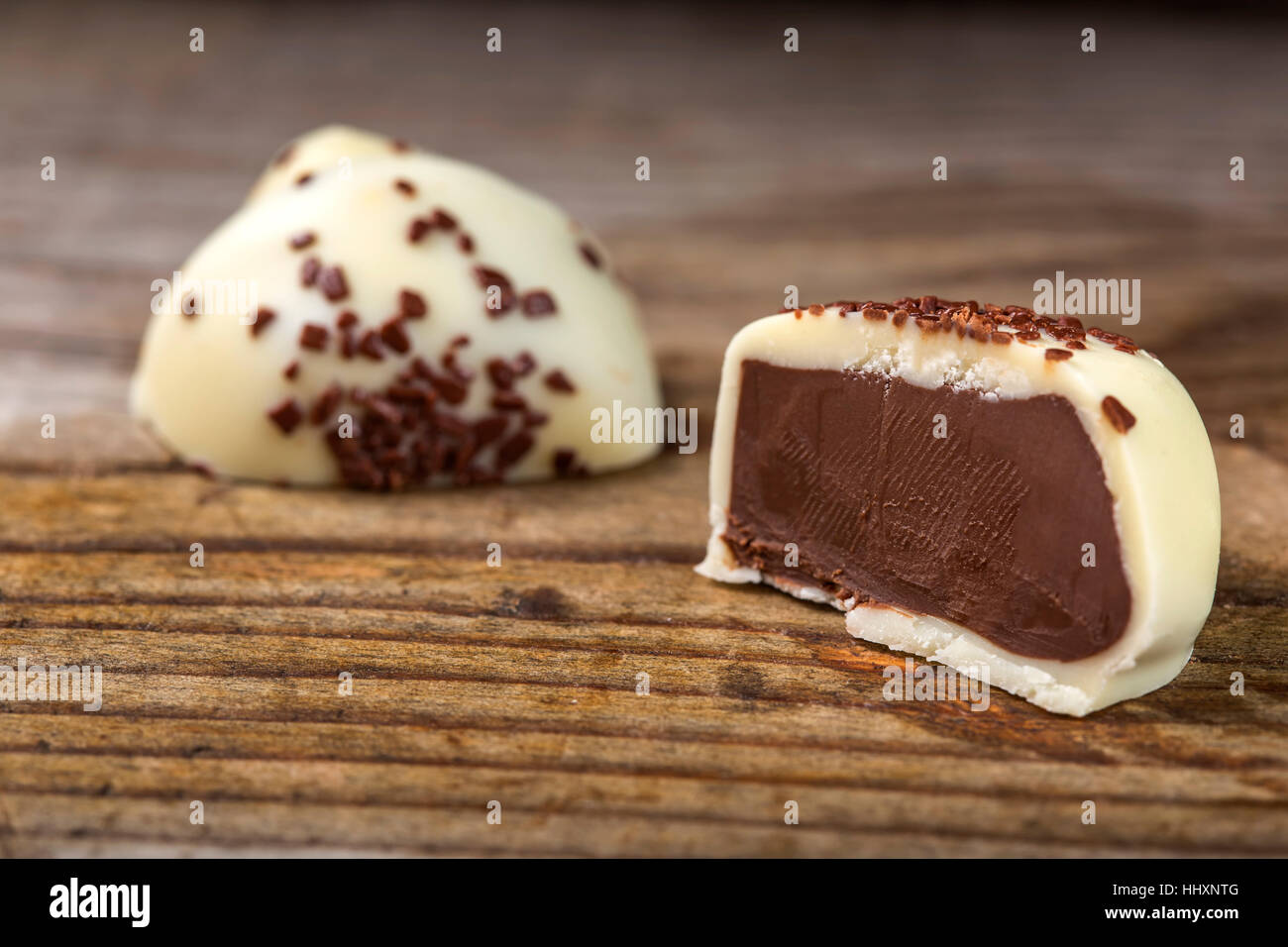 Un cioccolato bianco candy riempito con crema scuro tagliato a metà su sfondo di legno Foto Stock