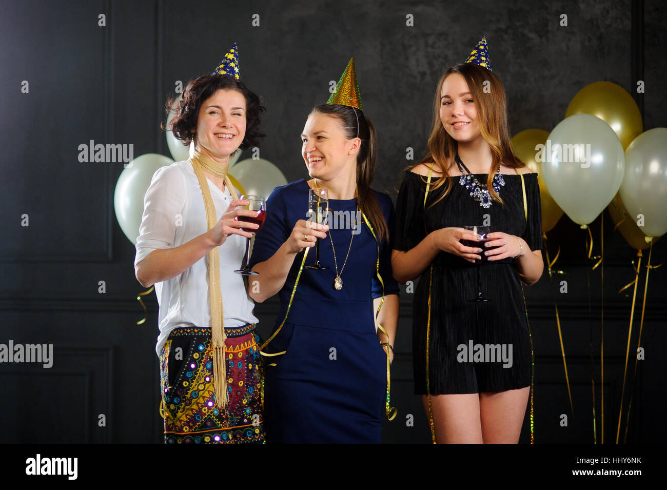 Tre giovani donne festeggiare qualcuno il compleanno. In mani a tutti con un bicchiere di champagne. Essi sono elegantemente vestito. Allegra festa di compleanno. Foto Stock