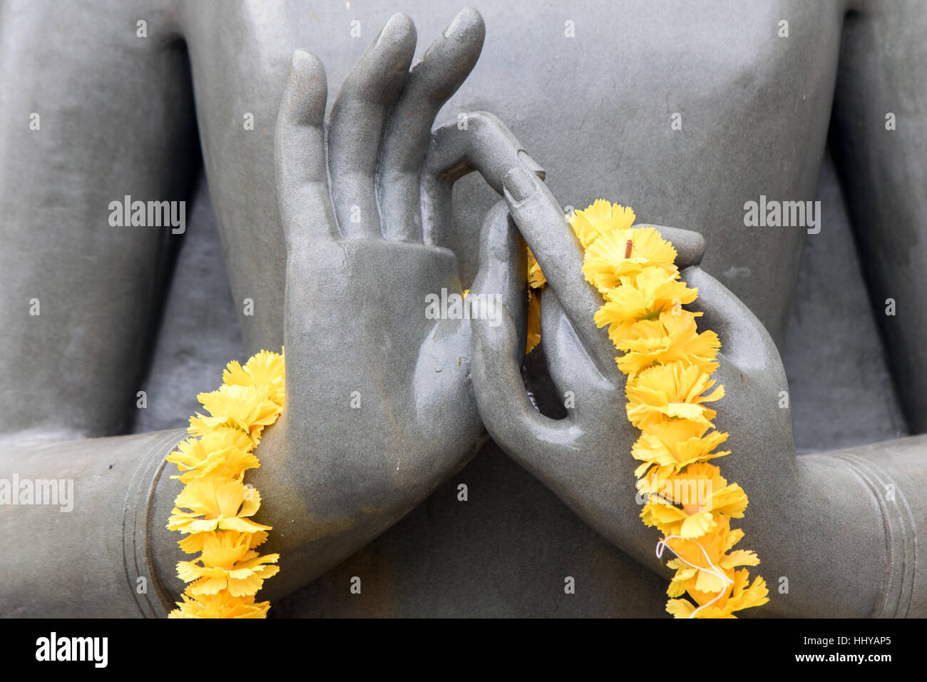 Il dettaglio della statua di Budda in posizione di meditazione. mani meditazione Buddha con una ghirlanda di fiori gialli. Foto Stock