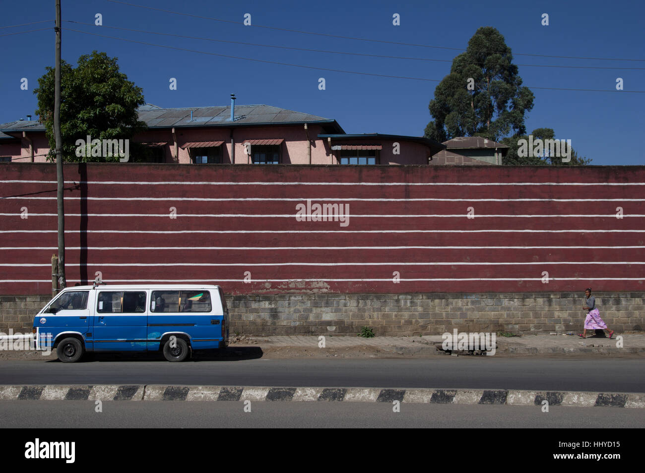 Rosso e bianco striscia orizzontale parete in Etiopia ad Addis Abeba, con blu e bianco van davanti e la donna in esecuzione in abito rosa Foto Stock