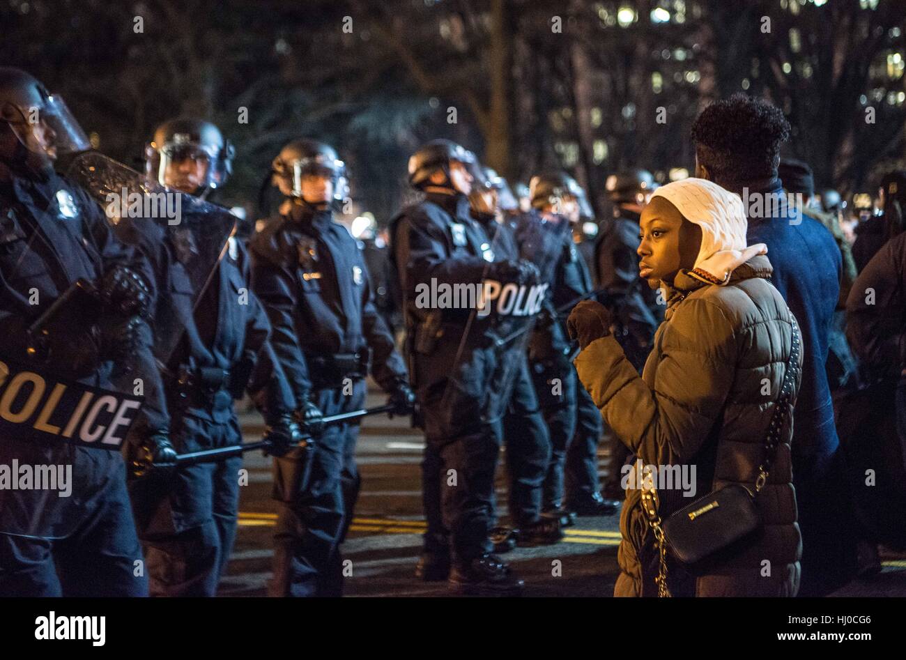 I manifestanti alla cerimonia di inaugurazione del presidente Donald Trump a Washington DC. Una giovane donna nera e il suo partner stand provocatoriamente, con un pugno fo solidarietà sollevata, nella parte anteriore della polizia vestito in combattimento tattico ingranaggio. Foto Stock