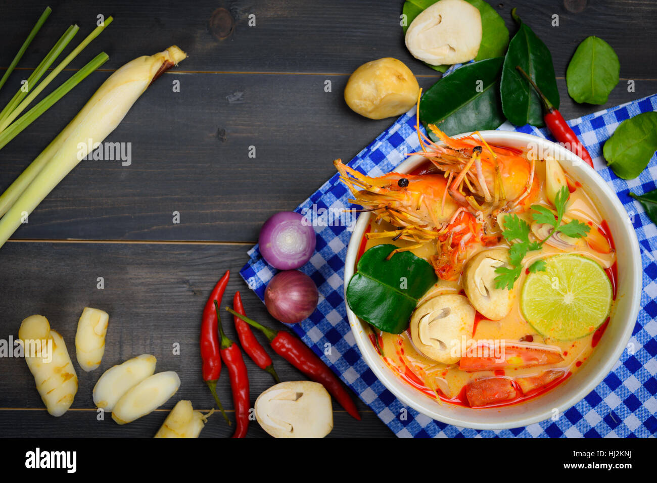 Tom Yum o zuppa di gamberi di fiume piccante minestra acida (Tom Yum Goong) sul tavolo di legno con tovaglia blu e vegetali vista superiore, Tailandese cibo locale Foto Stock