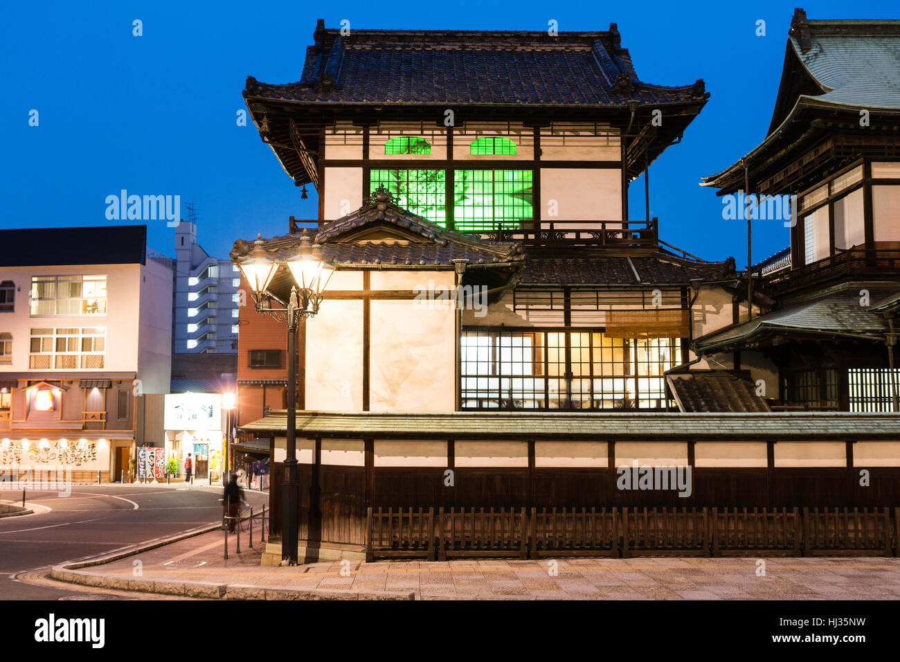 Giappone, Matsuyama. Periodo Meiji edificio in legno il famoso Dogo Onsen bathhouse. Parete e edificio principale. Notte tempo. Foto Stock