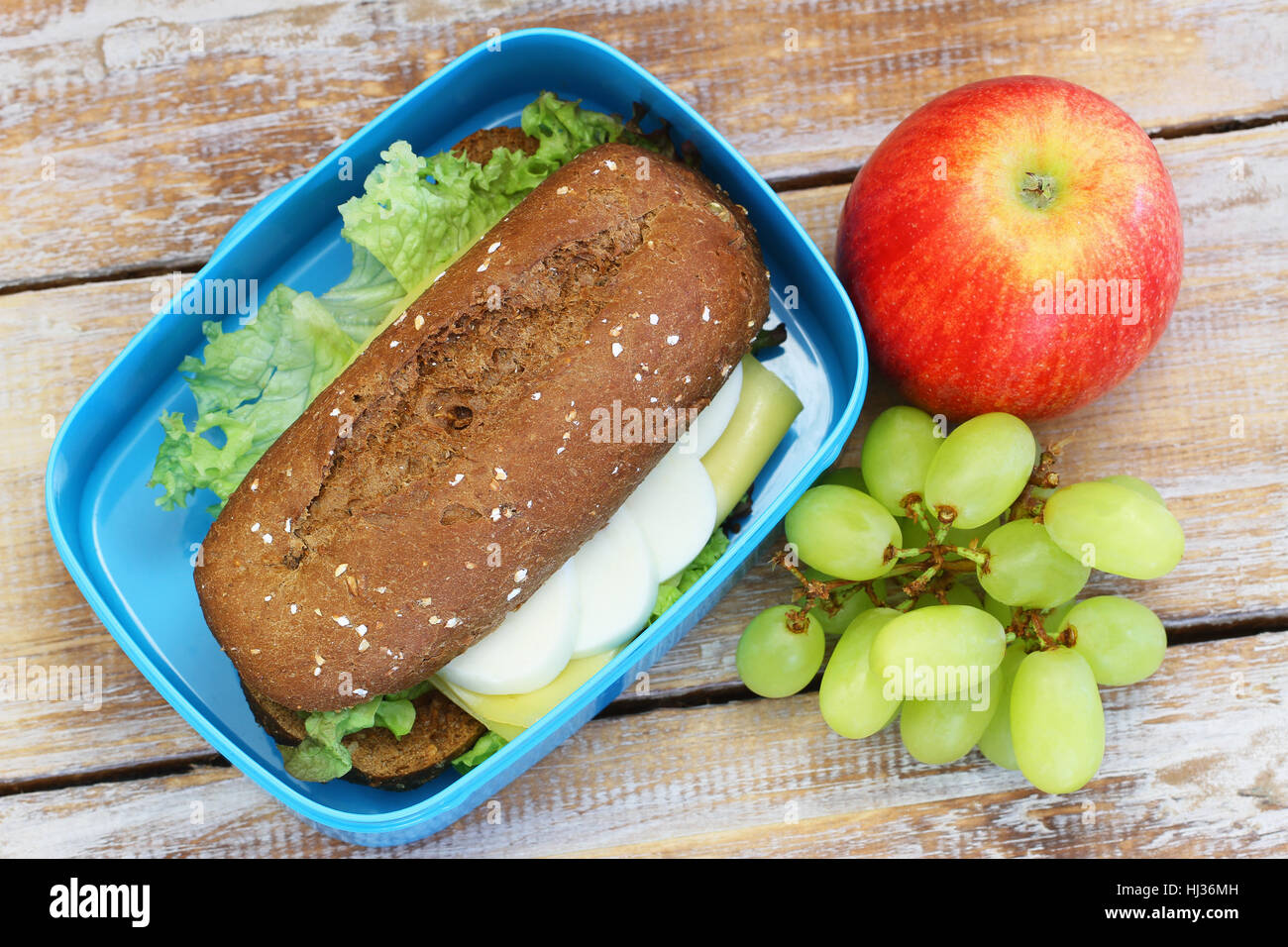Pranzo sano scatola contenente marrone Rotolo di pane con formaggio, uovo sodo e lattuga, uva e mela rossa Foto Stock