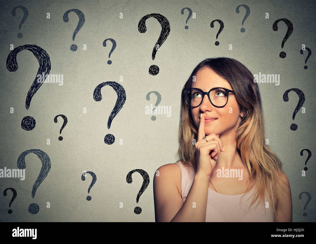 Pensa business donna con gli occhiali alla ricerca fino a molte domande mark isolato sul muro grigio sfondo Foto Stock