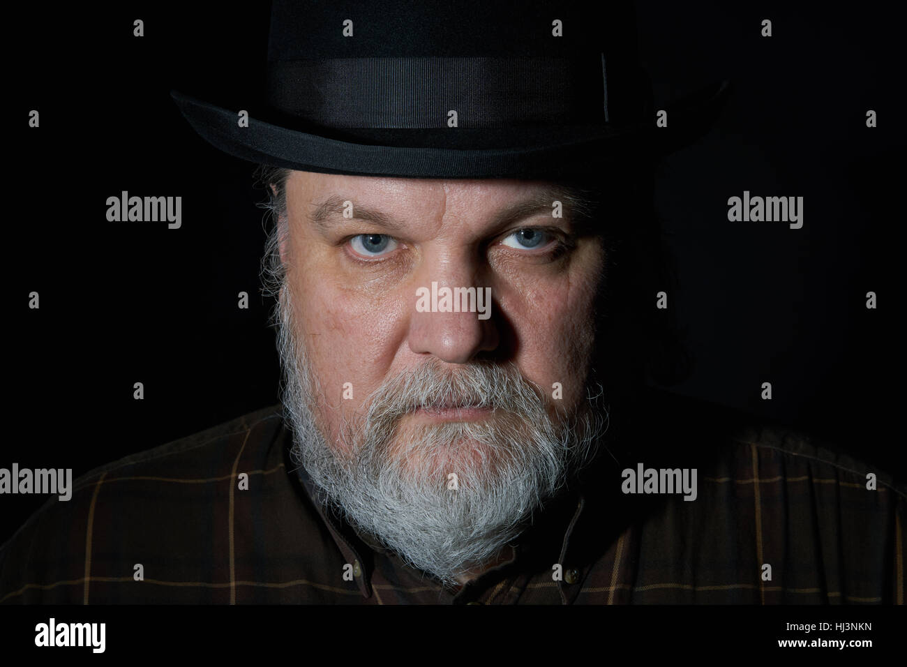 Ritratto di uomo con barba grigia nel cappello nero su sfondo nero Foto Stock