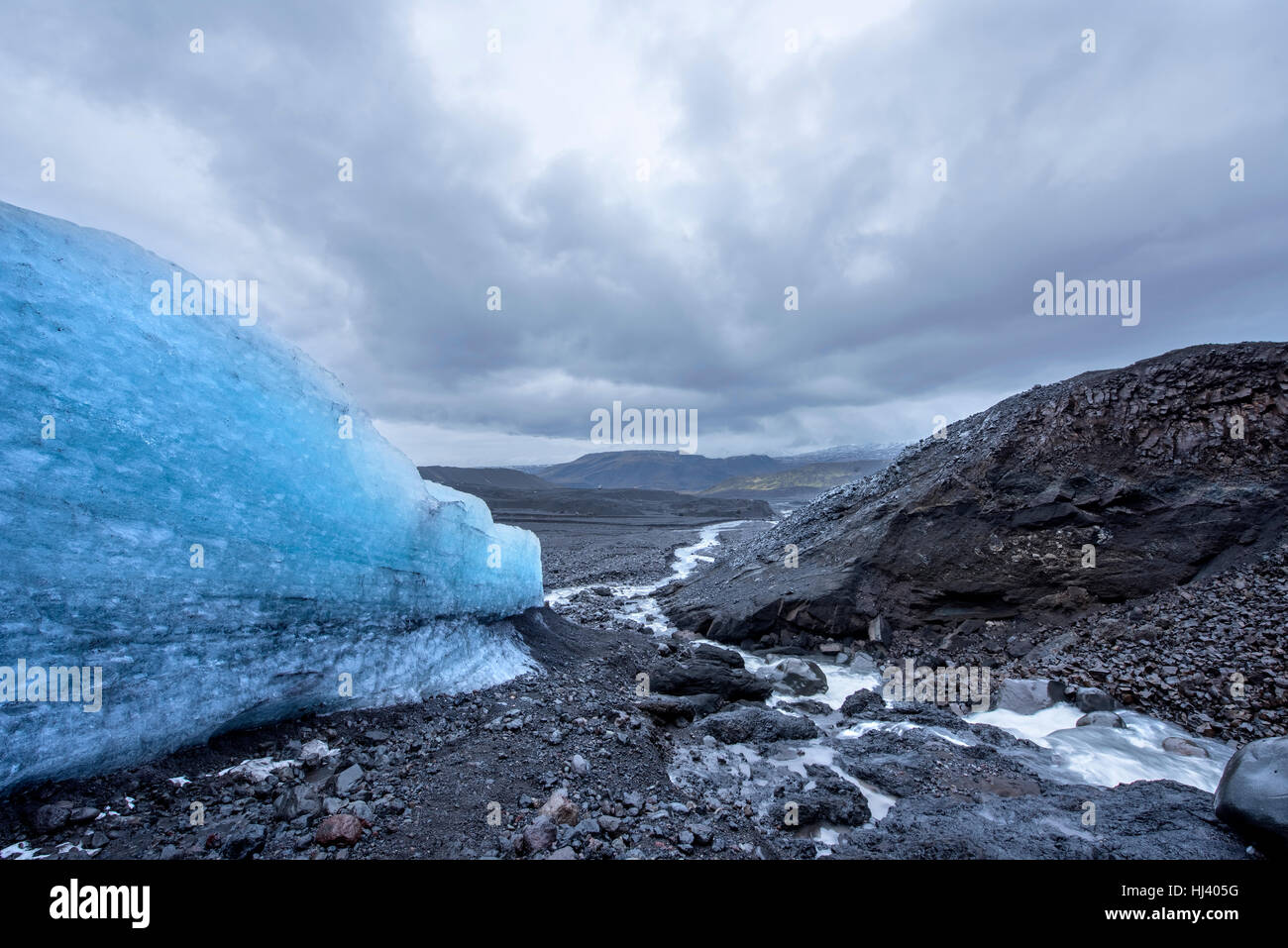 Il lato di un ghiacciaio di fusione in un robusto Islanda deserto forma un piccolo ruscello in giù per il pendio della montagna durante un grigio e nuvoloso giorno. Foto Stock