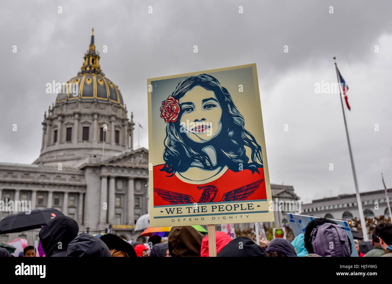 San Francisco, California, Stati Uniti d'America. Il 21 gennaio, 2017. Le donne di marzo - Artista Shepard Fairey il segno "siamo il popolo a difendere la dignità", raffigurante un Latina in rosso, è tenuta in alto in segno di protesta per il rally prima di San Francisco Womens Marzo con City Hall in background. Credito: Shelly Rivoli/Alamy Live News Foto Stock