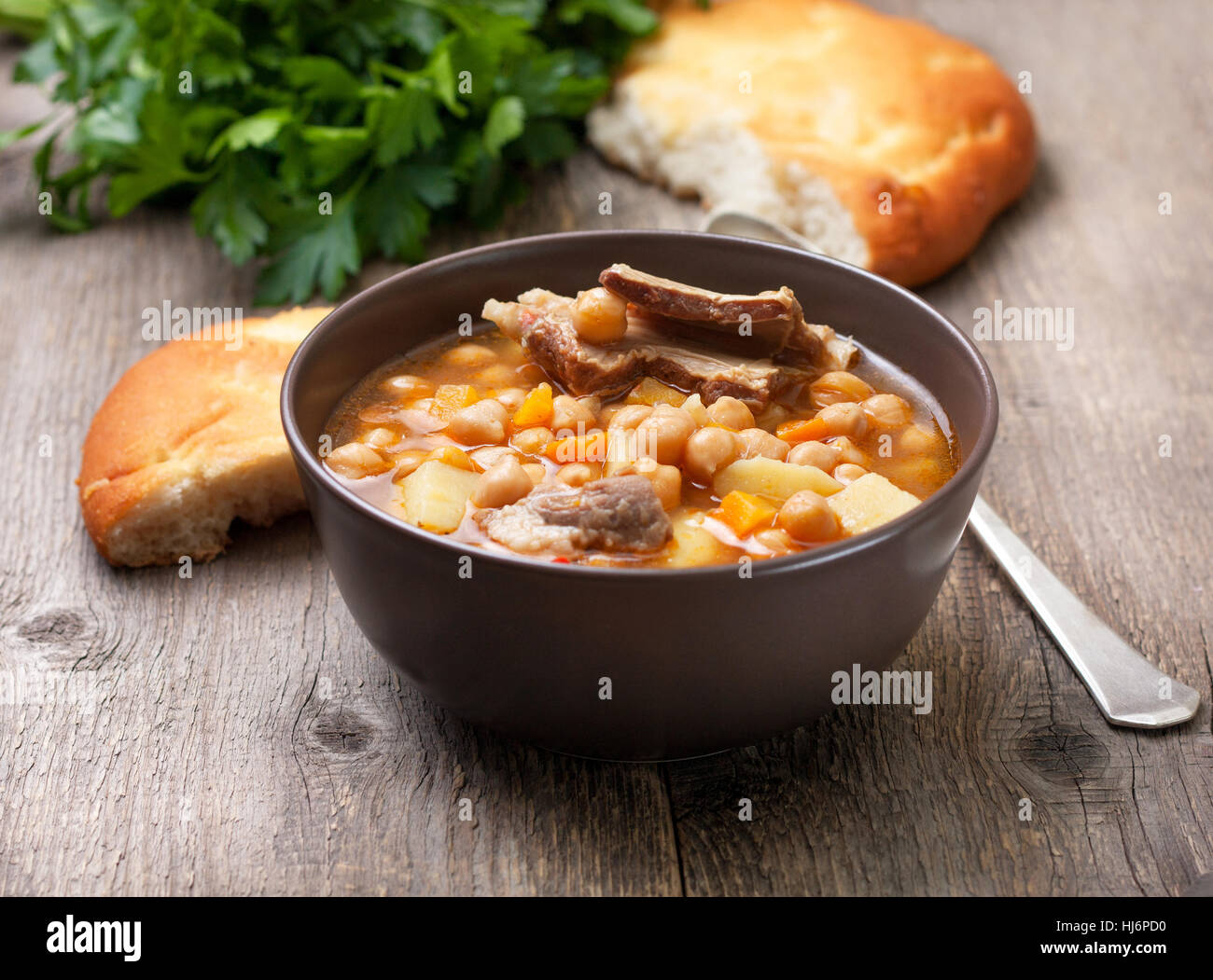 Zuppa di agnello i ceci in una terrina, il prezzemolo e il pane piatto sul vecchio sfondo di legno Foto Stock