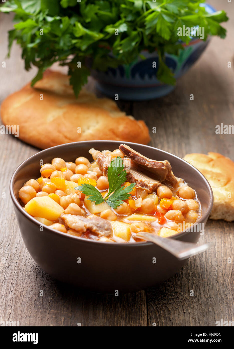 Zuppa di agnello i ceci in una terrina, il prezzemolo e il pane piatto sul vecchio sfondo di legno Foto Stock