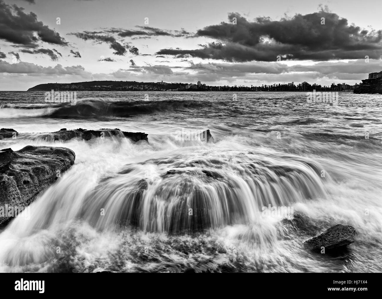 Drammatica forte ondata trabocca oltre il masso di arenaria a Freshwater Beach a nord di Manly a Sydney, in Australia. Nero-bianco di conversione stormy sunset Foto Stock
