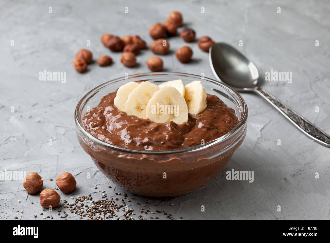 Il cioccolato alle nocciole budino di Chia con banana in una ciotola di vetro sul cemento grigio sfondo Foto Stock