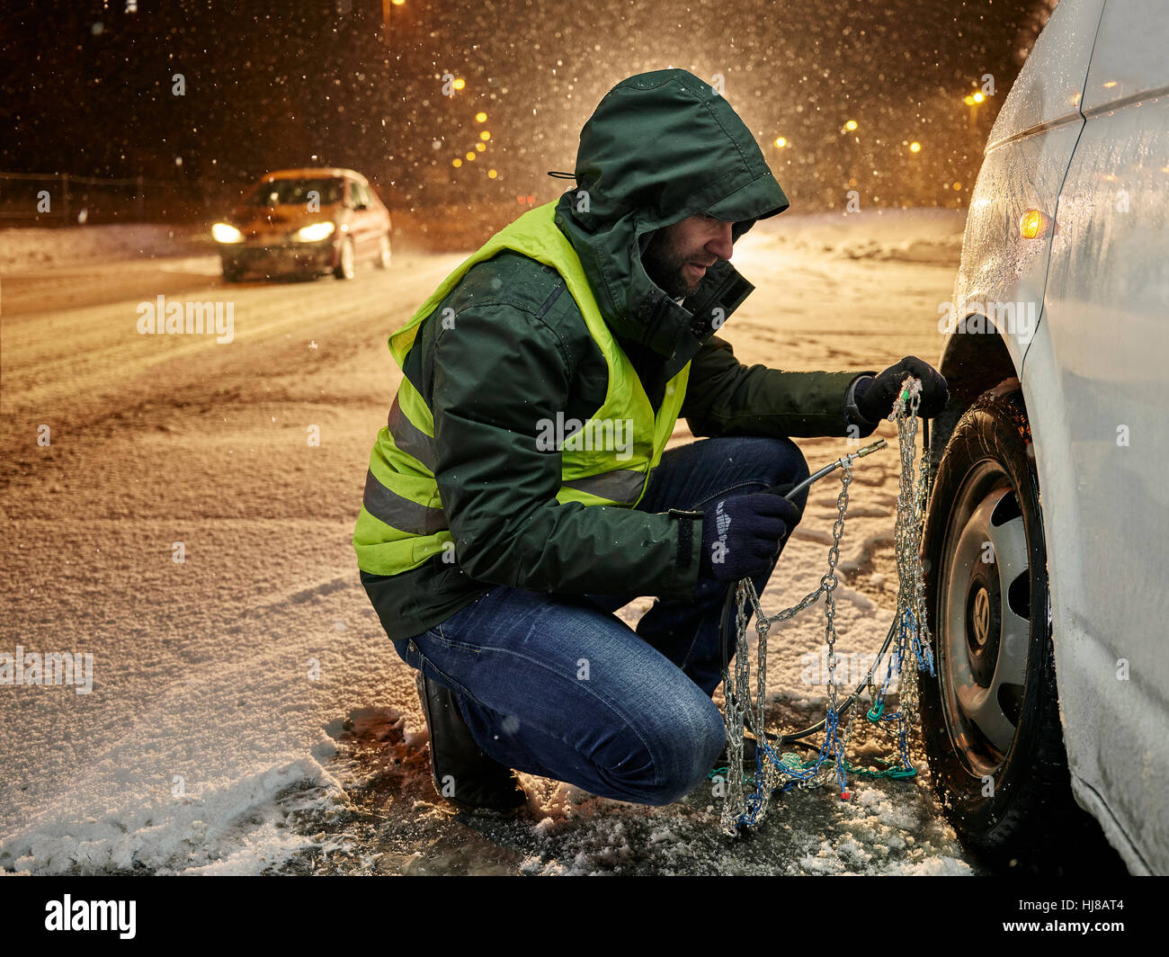 Uomo con giubbotto di sicurezza applicando le catene da neve su neve road, Wattens, Tirolo, Austria Foto Stock