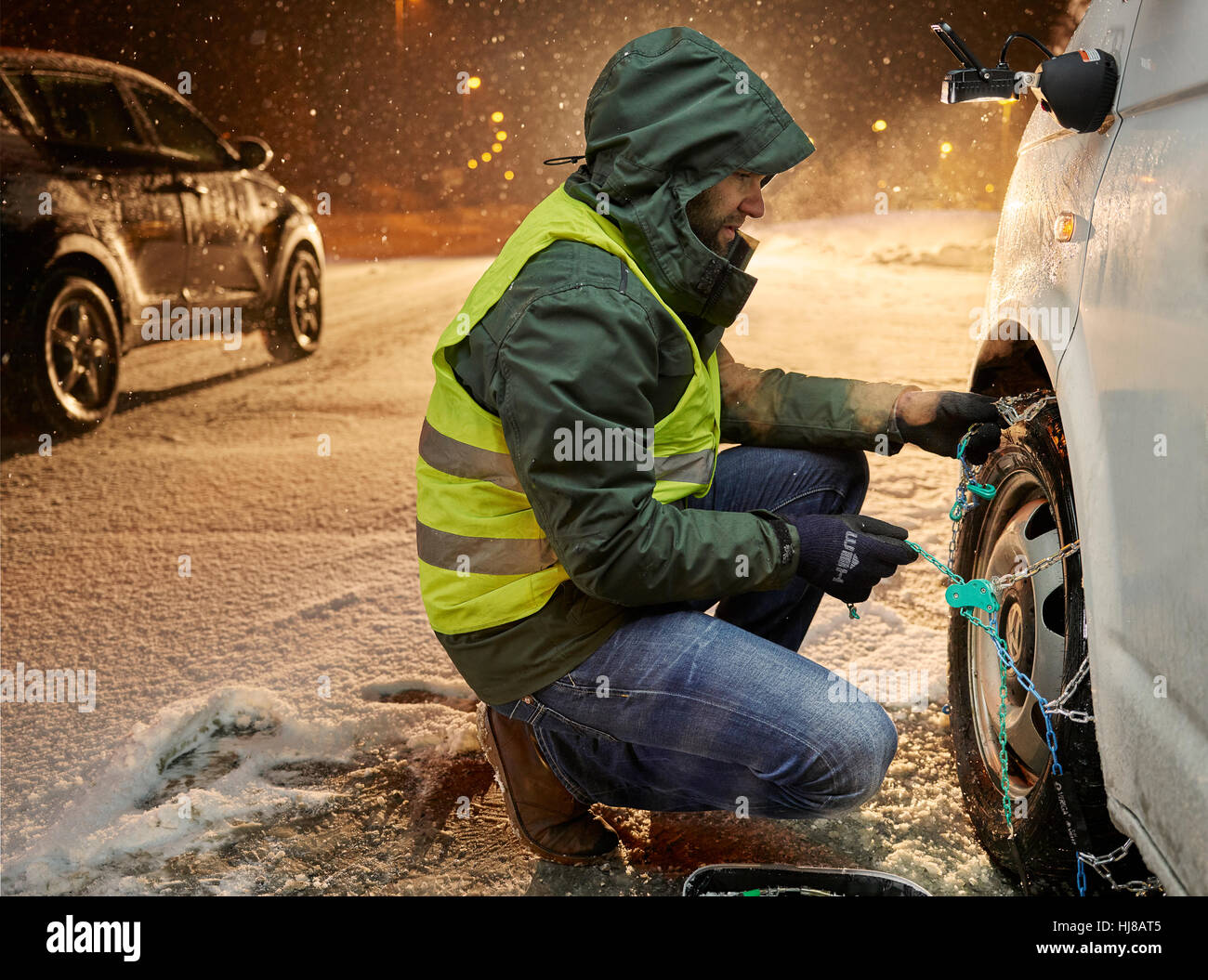 Uomo con giubbotto di sicurezza applicando le catene da neve su neve road, Wattens, Tirolo, Austria Foto Stock