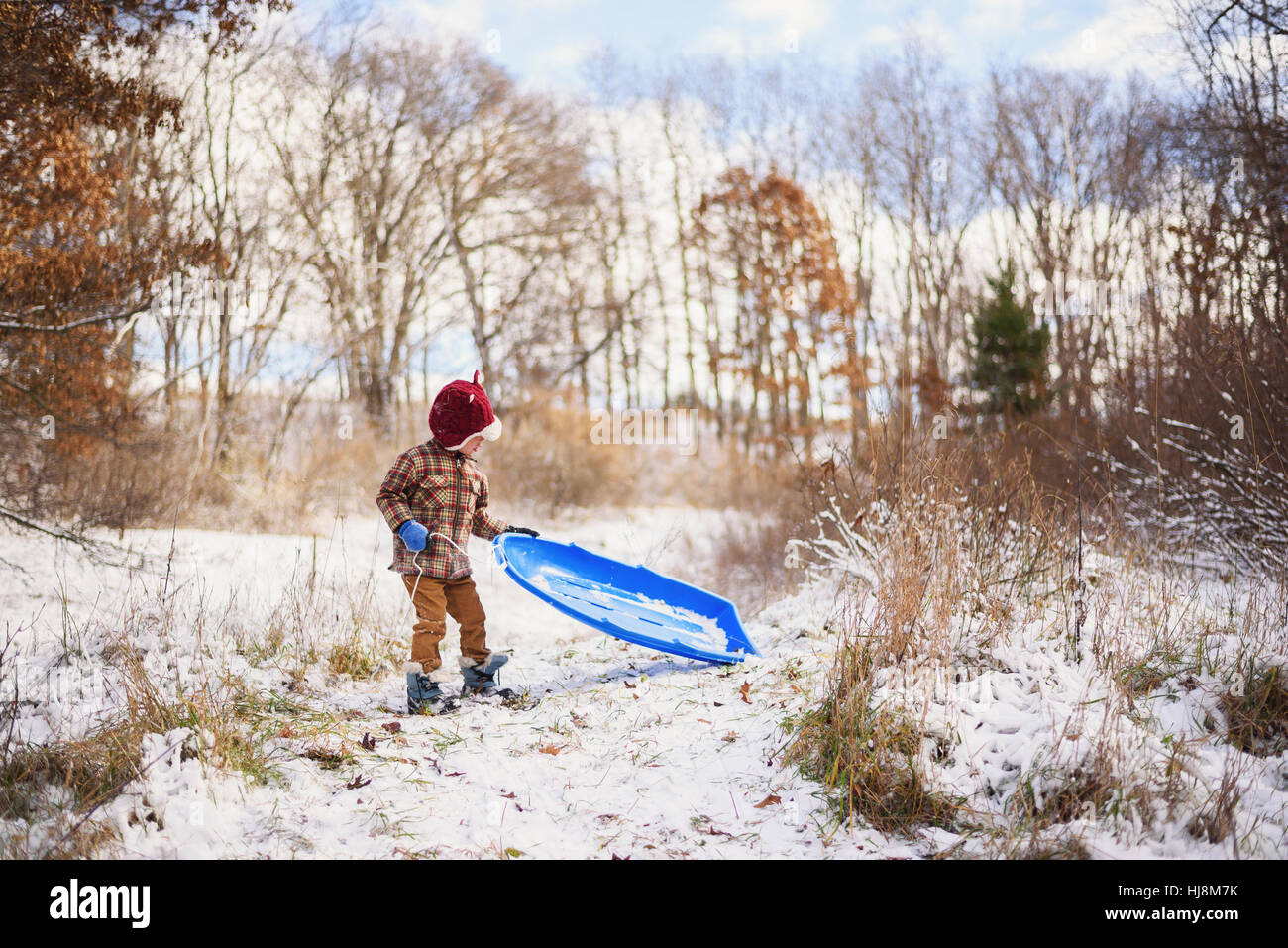 Ragazzo in piedi nella neve con la sua slitta Foto Stock