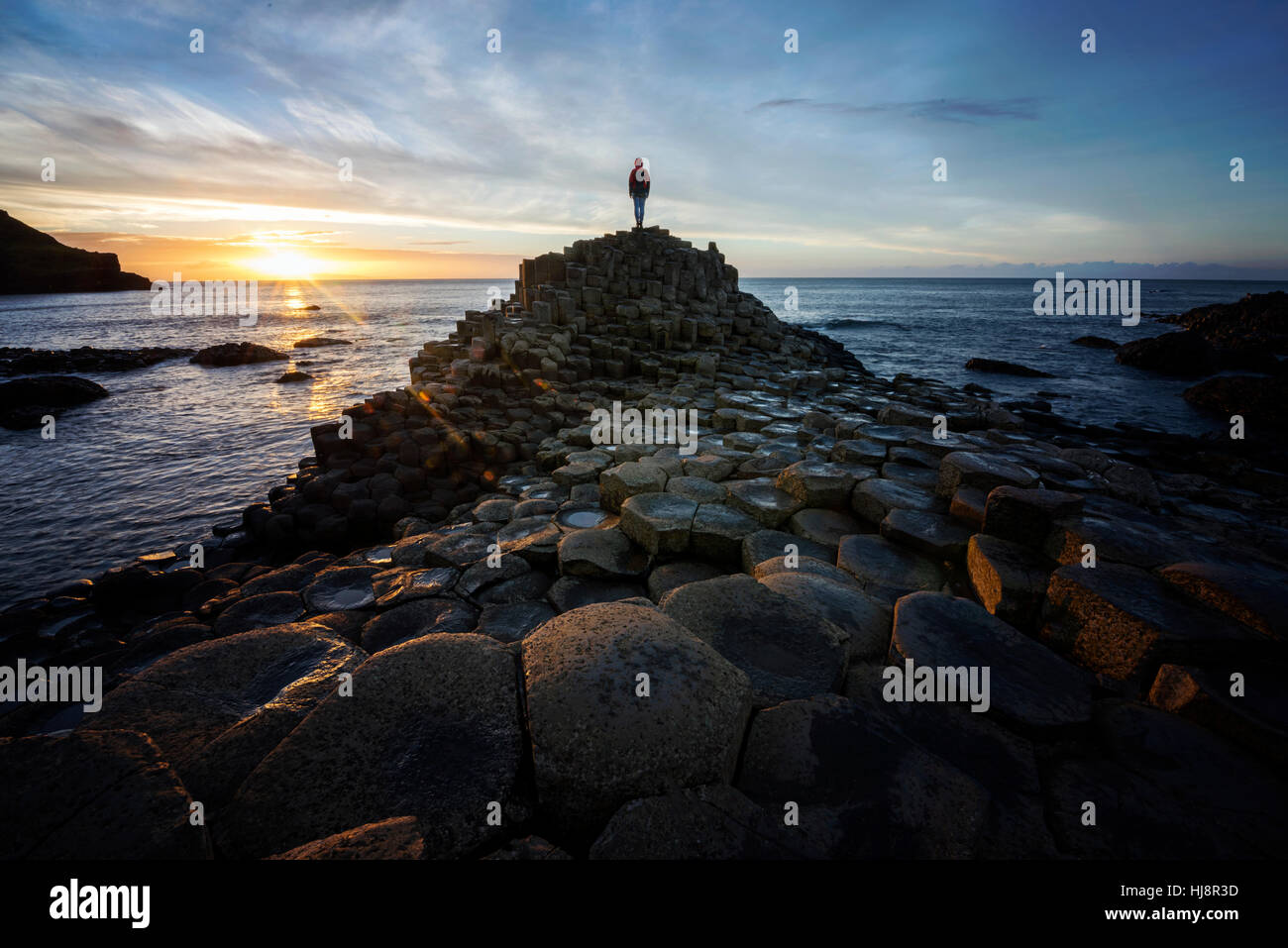 Donna che si trova sul Selciato dei Giganti al tramonto, contea di antrim, Irlanda del Nord, Regno Unito Foto Stock