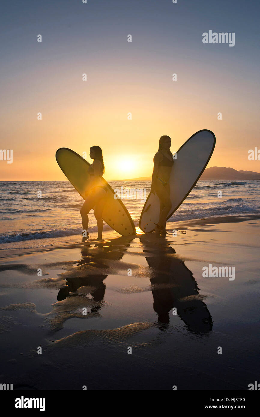 Due donne sulla spiaggia che trasportano le tavole da surf al tramonto, Los Lances Tarifa, Cadice, Andalusia, Spagna Foto Stock